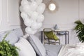 Olive green pillow on fancy golden armchair in chic bedroom with bunch of white balloons, copy space on the empty wall