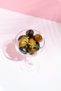 Olive Kalamata in cocktail glass. Black and green olives food on white table with pink wall. Day sunlight with hard shadow of fern
