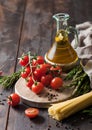 Olive oil with cherry tomatoes on round chopping board and with spaghetti pasta and rosemary and asparagus on wooden background Royalty Free Stock Photo