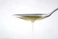olive oil drop from a silver spoon against white background
