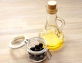 Olive Oil in figured bottle with fresh marinated black olives in glass jar on wooden background view