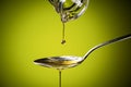 Olive oil flowing on spoon on green background