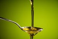 Olive oil flowing on spoon on green background