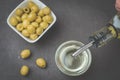 Olive oil pouring from bottle in bowl and fresh olives in ceramic plate and on dark stone table. Top view Royalty Free Stock Photo