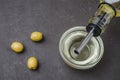 Olive oil pouring from bottle in bowl and fresh olives in ceramic plate and on dark stone table. Top view Royalty Free Stock Photo