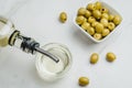 Olive oil pouring from bottle in bowl and fresh olives in ceramic plate and on white stone background. Top view Royalty Free Stock Photo