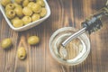 Olive oil pouring from bottle in bowl and fresh olives in ceramic plate and on wooden background. Top view Royalty Free Stock Photo