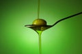 Olive oil in a spoon overflowing on green background Royalty Free Stock Photo