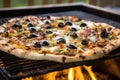 olive topped bbq pizza baking on a grill with visible fire