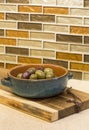 Olives in bowl and wooden cutting board on engineered stone countertop with glass mosaic tile backsplash in home kitchen Royalty Free Stock Photo