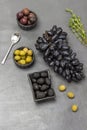 Olives in bowls. Bunch of black grapes, sprig of thyme and spoon on table