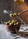 Olives in wooden spoon pouring oil over bowl full of olives with bone