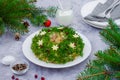 Olivier salad Christmas wreath with vegetables, meat, eggs and mayonnaise on a plate on a gray background.