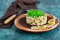 Olivier salad with greens on top and lemons, served on an unusual clay plate with a pattern, a portion of a well-known dish in an