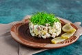 Olivier salad with greens on top and lemons, served on an unusual clay plate with a pattern, a portion of a well-known dish in an