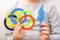 Olympics, Japan, Tokyo, summer, 2020. A child`s hand holds multi-colored rings and a blue torch made of cardboard