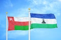 Oman and Lesotho two flags on flagpoles and blue sky