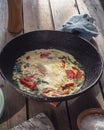 Omelet with tomatoes in a round cast iron pan on an old Board table, a napkin with a pattern and a large salt in a salt