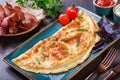 Omelette with prosciutto, slices ham, mushrooms, greens, cheese and tomato sauce on dark wooden background. Royalty Free Stock Photo