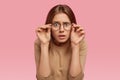Omg, I dont believe you. Shocked emotional dark haired woman keeps hands on rim of spectacles, gazes with stupefaction Royalty Free Stock Photo