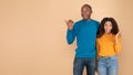Omg, look here. Excited black couple demonstrating place for your text, beige background, panorama, copy space