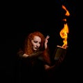 An ominous witch sets her spell book on fire with the power of thought. Red-haired woman conjures for Halloween. Flames Royalty Free Stock Photo