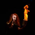 An ominous witch sets her spell book on fire with the power of thought. Red-haired woman conjures for Halloween. Flames Royalty Free Stock Photo