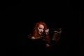 An ominous witch sets her spell book on fire with the power of thought. Red-haired woman conjures for Halloween. Flames Royalty Free Stock Photo