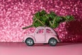 Omsk, Russia - Oktober 27, 2018: toy model car with Christmas tree on on the roof rides on pink Blurred Glitter background. Royalty Free Stock Photo