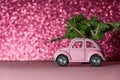 Omsk, Russia - Oktober 27, 2018: toy model car with Christmas tree on on the roof rides on pink Blurred Glitter background. Royalty Free Stock Photo