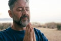 One adult man praying and meditate outdoor in relaxation gesture with hands clasped and closed eyes portrait. Zen like healthy