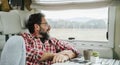 One adult man relaxing inside a camper modern motorhome looking outside the window enjoyuing the wild nature view. Alternative