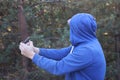 one aggressive male criminal in blue clothes and a hood holds a large brown rusty machete knife in his hands on the street