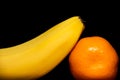 One banana and mandarin on a black background is close Royalty Free Stock Photo