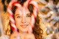 One beautiful curly-haired girl stands near the tree, New Year photo session with candy lollipop Royalty Free Stock Photo