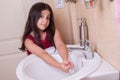 One beautiful little middle eastern arab girl with red dress is washing her hands in the bathroom.