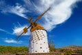 One beautiful spanish isolated ancient white traditional stone windmill, brown wood wings against blue sky, few scattered fluffy