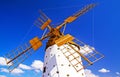 One beautiful spanish isolated ancient white traditional stone windmill, brown wood wings against blue sky, few scattered fluffy