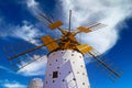 One beautiful spanish isolated ancient white traditional stone windmill, brown wood wings against blue sky, few scattered fluffy