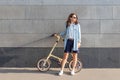 One beautiful woman stands near a stone wall and holds a folding bike.