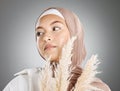 One beautiful young muslim woman wearing brown headscarf holding a pampas wheat plant isolated against grey studio Royalty Free Stock Photo