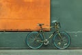 One bicycle in front of steel orange door with green wall of warehouse