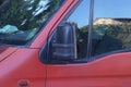 One big black plastic car mirror next to the gray glass of a red auto