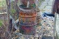 A big old rusty brown barrel with garbage is standing on the street near the fence
