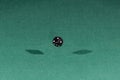 One black dice falling on a green table