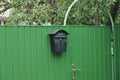 One black iron mailbox hangs on a green metal fence