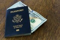 Blue American passport with some US dollars on top of a wooden desk