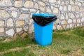 A blue plastic trash can with a black plastic bag near a decorative stone wall Royalty Free Stock Photo