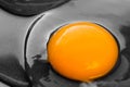 One bright round yolk in raw whites, uncooked small fried eggs is a simple breakfast in a black skillet.