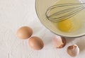 One broken egg in a Cup with a whisk and two whole eggs with a shell on a white surface Royalty Free Stock Photo